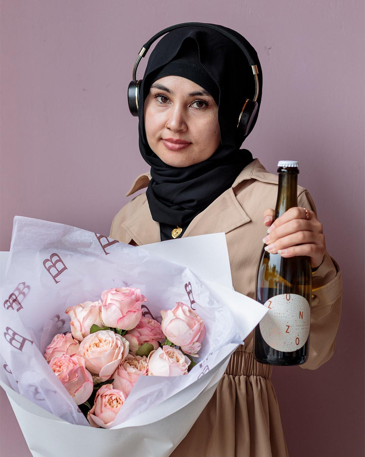 Woman holding a bouquet of pink roses and a bottle against a plain background