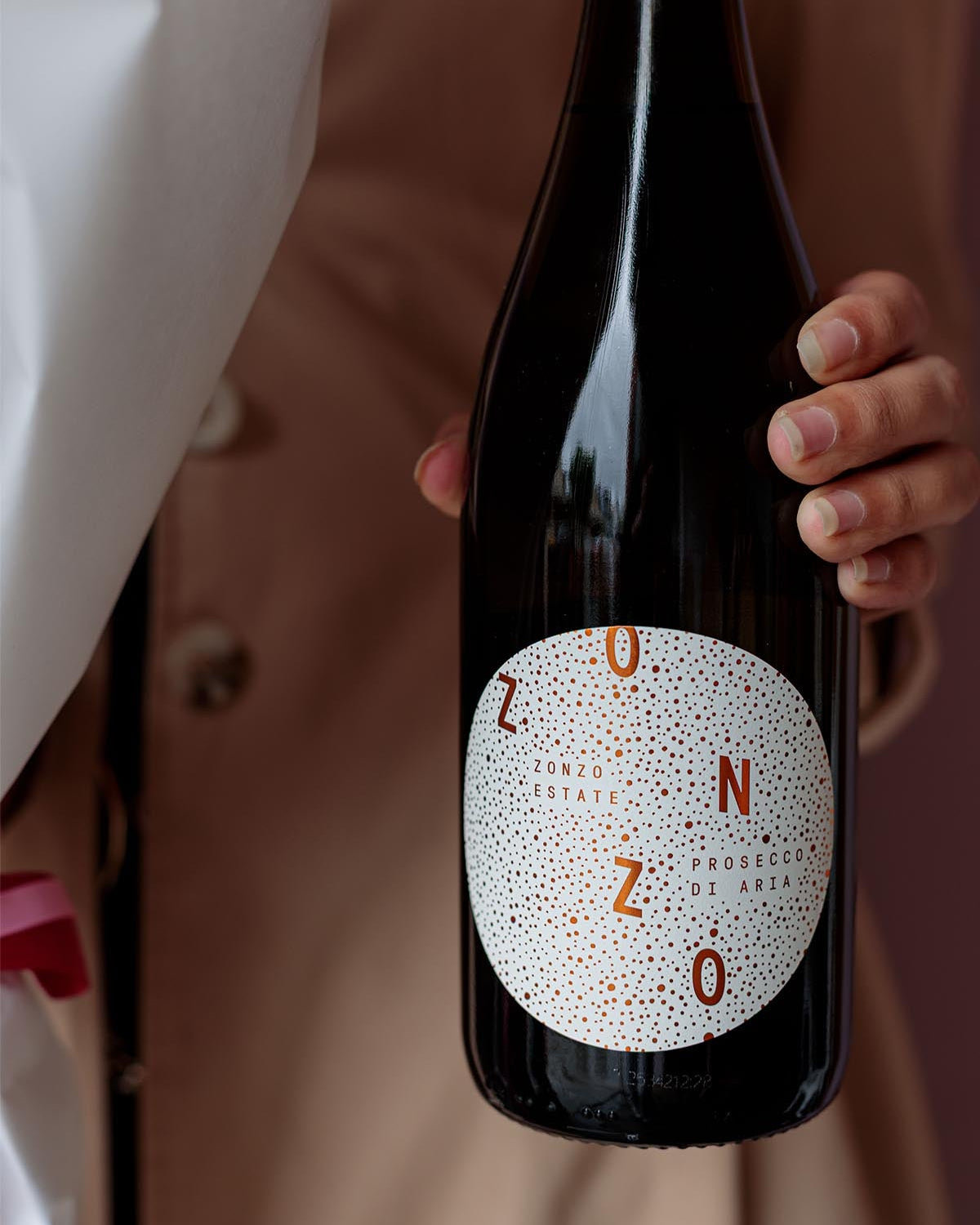 Person holding a bottle of Zonzo wine with a white label.
